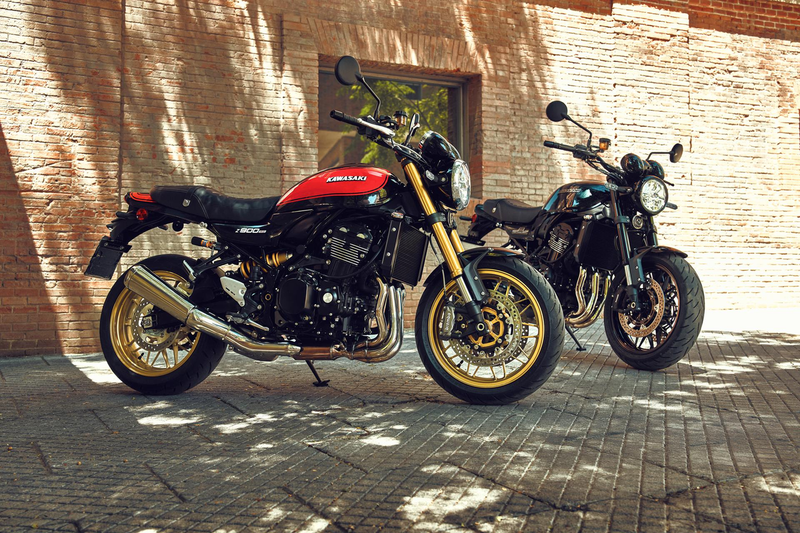 Load image into Gallery viewer, Two Kawasaki Z900RS motorcycles parked side by side on a cobblestone street in front of a brick wall, with dappled sunlight and shadows across the scene.