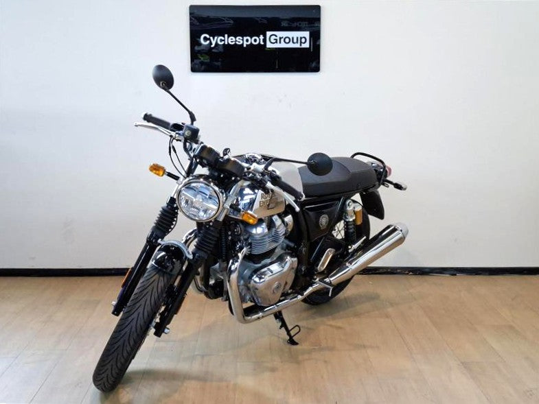 Load image into Gallery viewer, A black and silver 2026 Royal Enfield Continental GT Classic motorcycle is parked indoors on a light wood floor against a white wall, with a 'Cyclespot Group' sign visible above it.