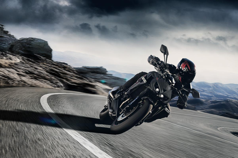 Load image into Gallery viewer, A green and black Kawasaki Z1000 motorcycle with a rider in full gear leaning into a curved mountain road under a dramatic cloudy sky.