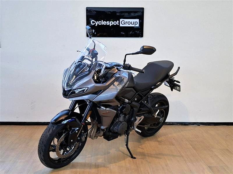 Load image into Gallery viewer, A grey 2023 Triumph Tiger Sport 660 motorcycle is parked indoors on a wooden floor against a white wall, with a 'Cyclespot Group' sign visible on the wall behind it.