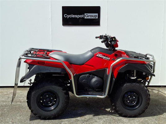 A red and black 2026 Suzuki KingQuad  LT-A500 four-wheeler ATV with a silver front bumper and rear rack, parked in front of a white wall with a 'Cyclespot Group' sign.