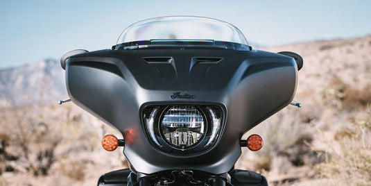 Front view of a 2026 Indian Chieftain Dark Horse motorcycle with a clear windshield and round headlight, set against a blurred desert landscape background.