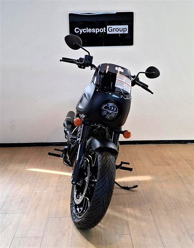 Load image into Gallery viewer, A black Indian Sport Chief cruiser motorcycle with a windscreen and orange turn signals, photographed indoors against a white wall with a 'Cyclespot Group' sign above it and light wood flooring.
