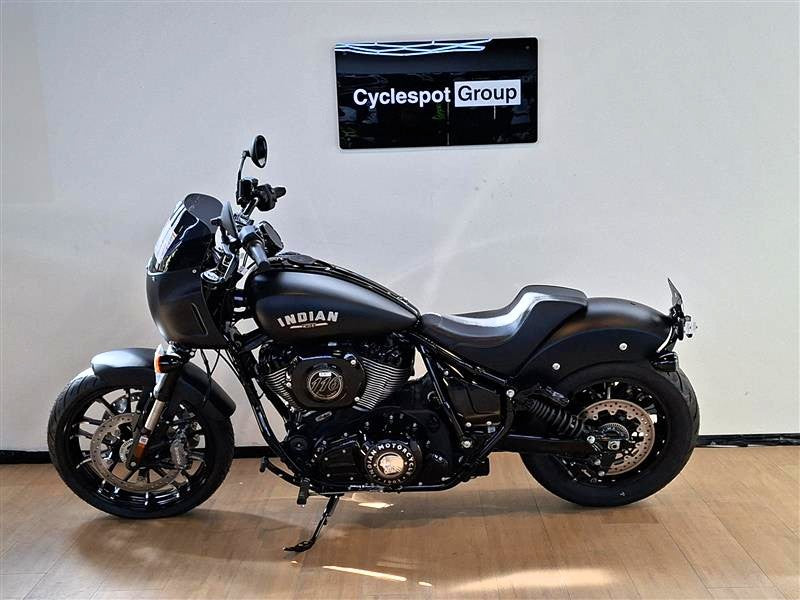 Load image into Gallery viewer, A black Indian Sport Chief motorcycle with chrome accents is parked indoors on a wooden floor against a white wall, with a sign reading 'Cyclespot Group' on the wall behind it.
