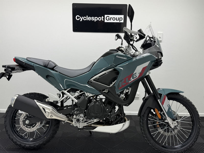Load image into Gallery viewer, A Kawasaki KLE adventure-touring motorcycle in a dark teal-gray color, photographed from the side against a light gray wall with a 'Cyclespot Group' sign in the background.
