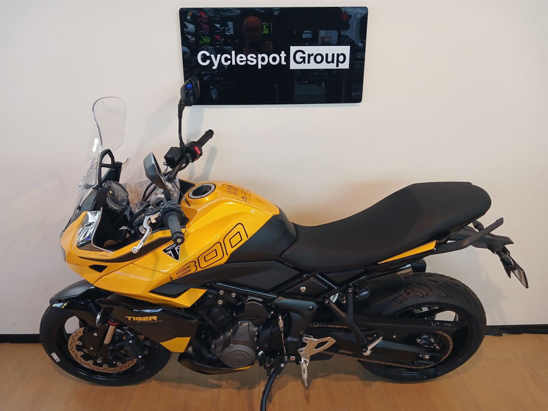 Load image into Gallery viewer, A yellow and black Triumph Tiger 800 motorcycle parked indoors against a beige wall, with a 'Cyclespot Group' sign visible above it.
