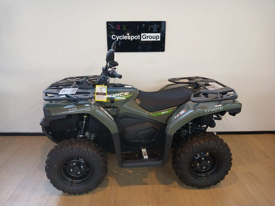 Left side of a green CF Moto C-Force 400 non-eps model on a wooden floor in front of a Cyclespot Group sign