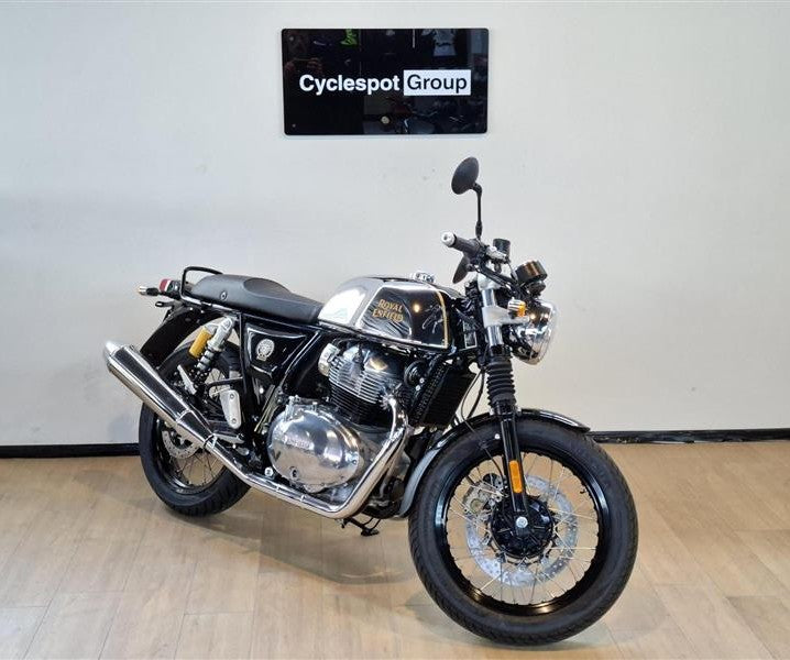 Load image into Gallery viewer, A 2026 Royal Enfield Continental GT Classic Cruiser motorcycle with a black and silver color scheme, parked indoors on a light wood floor against a white wall with a 'Cyclespot Group' sign above it.
