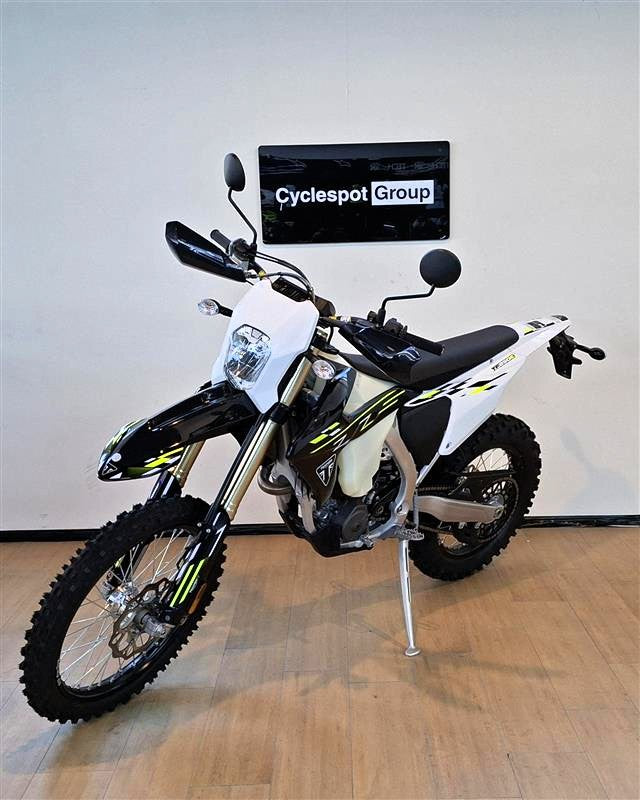 Load image into Gallery viewer, A white and black Triumph TF 250 E dirt bike with yellow accents, parked on a wooden floor against a white wall with a 'Cyclespot Group' sign.

