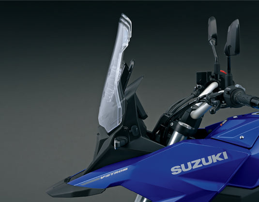 Close-up of a blue Suzuki V-Strom motorcycle showing the clear windshield, handlebars, mirrors, and side fairing against a dark studio background.