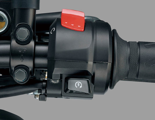 Close-up of a motorcycle handlebar control assembly with a black switch housing, a red quick-start switch, and a black handlebar grip on a gray background.
