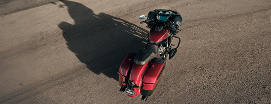 A red 2026 Indian Challenger 125th Anniversary motorcycle with black saddlebags and a windshield, photographed from a high-angle aerial perspective on a dusty, light-brown gravel surface.