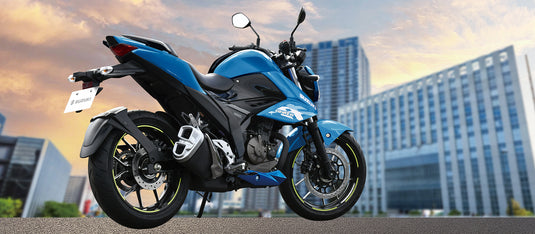 A blue and white 2025 Suzuki GSX 250 LAMS sport motorcycle parked outdoors on a paved surface with blurred modern buildings in the background under a warm sky.